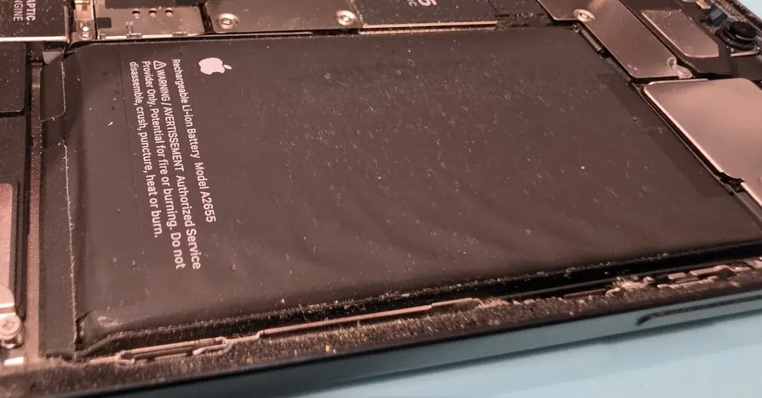 Swollen iPhone 13 battery bulging inside the opened phone on the bench, ready for a battery replacement
